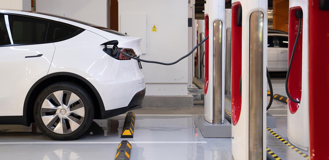 Back end of an electric car attached by to a charger stand by a large cord.