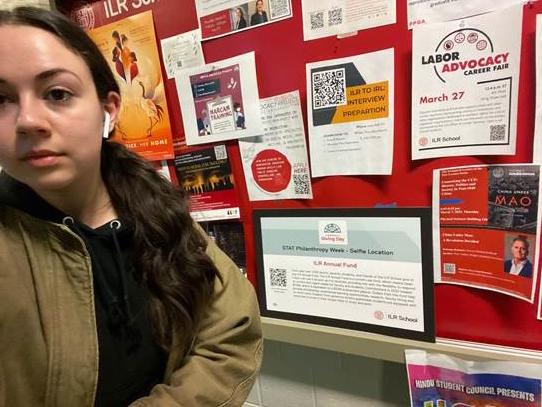 Emma Branft standing in from on a bulletin board covered with flyers