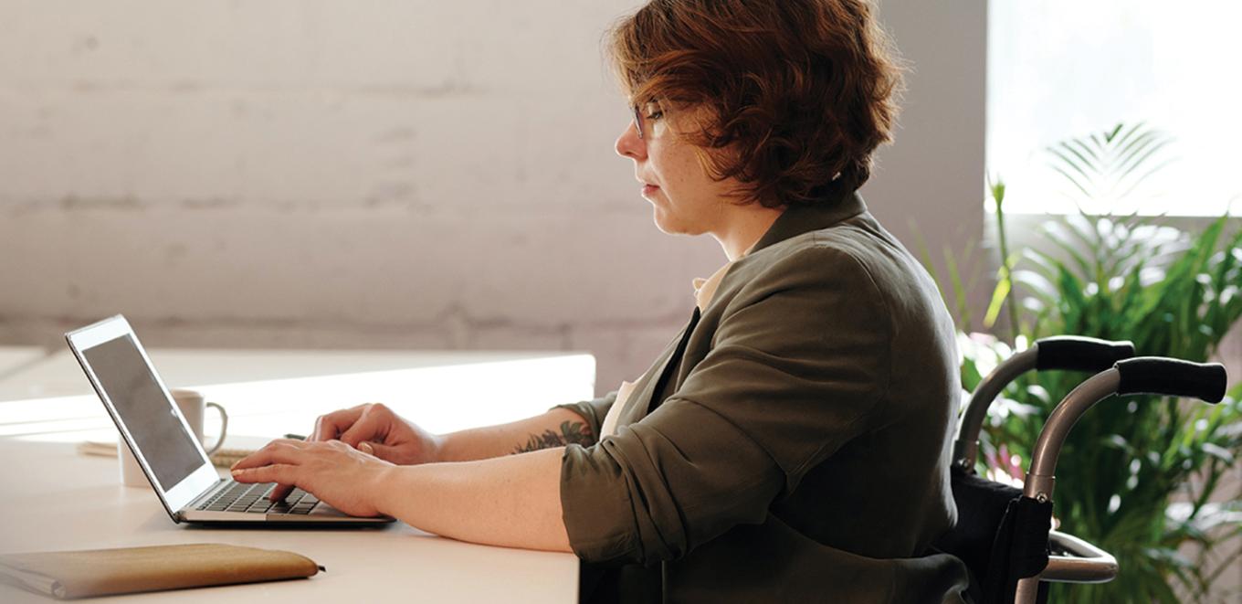 woman sitting in a wheelchair working at a desk with a laptop