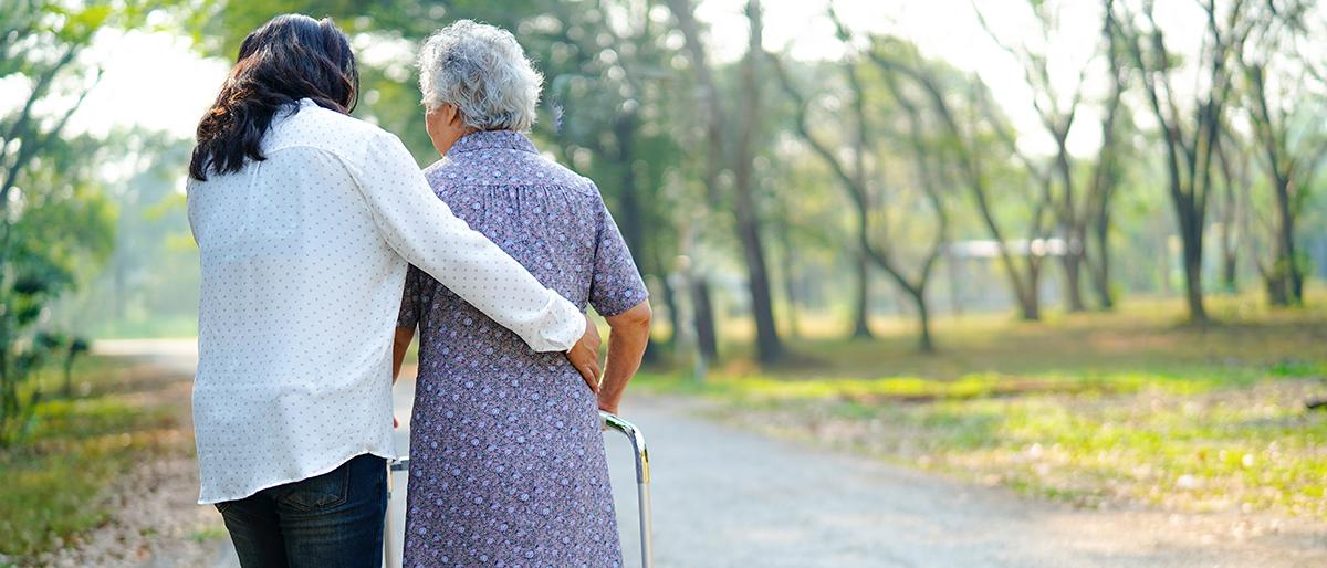 Older woman outside with a walker assisted by a home health aide