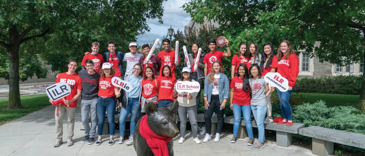 Large group of ILR students posing by Touchdown the Bear statue during Cornell Homecoming.