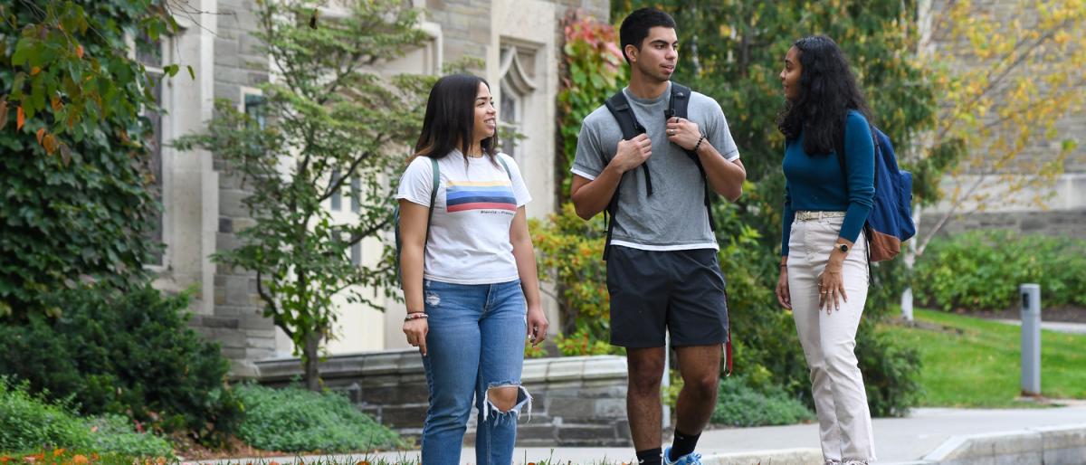 Three students standing and chatting outside with the ILR School in the background..
