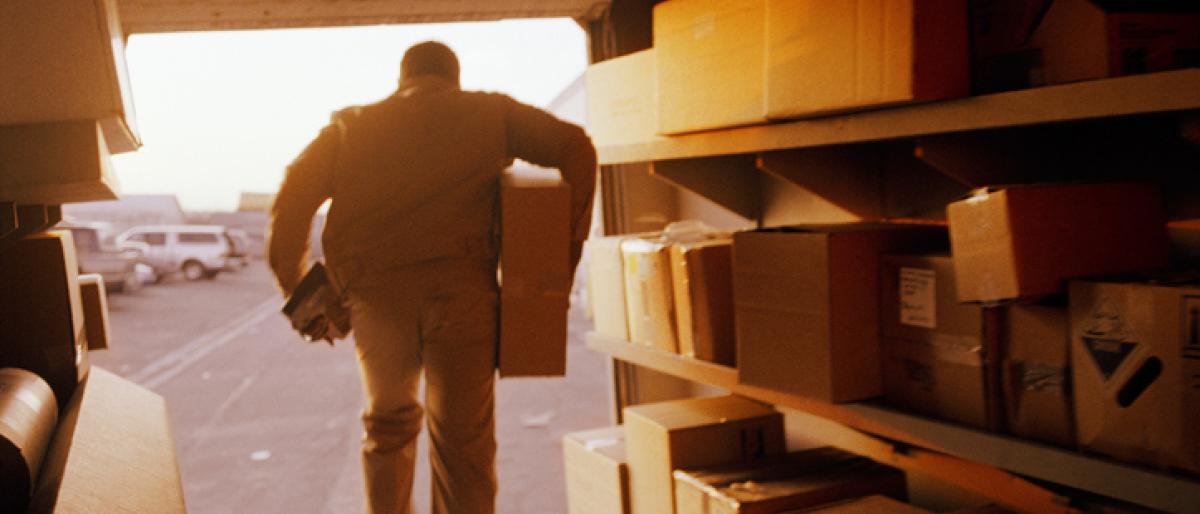 Male delivery person carrying a parcel out of the back of a truck filled with parcels