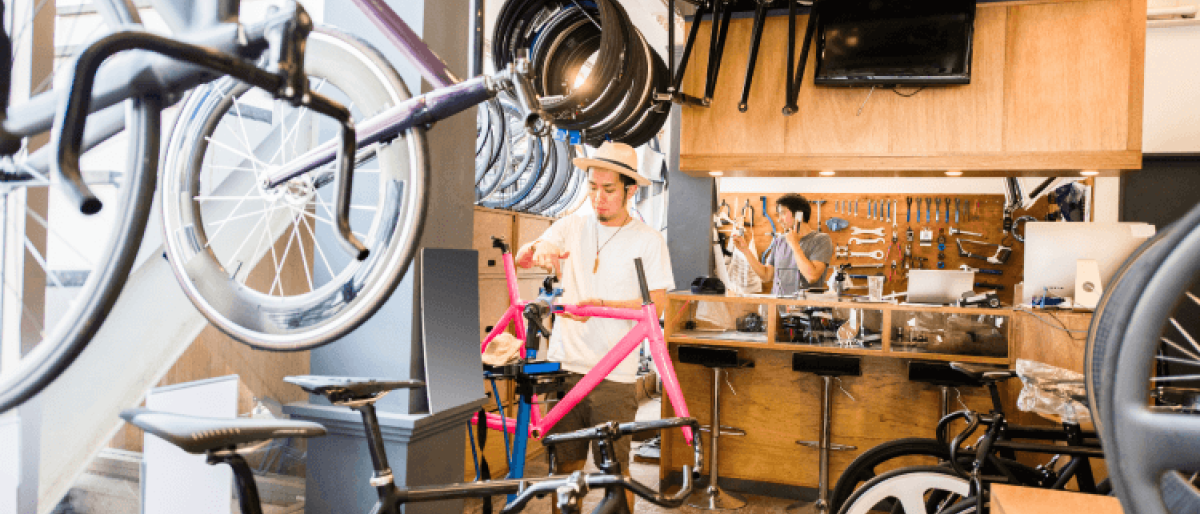 Two workers in a shop, surrounded by bicycle tires, tools, and equipment