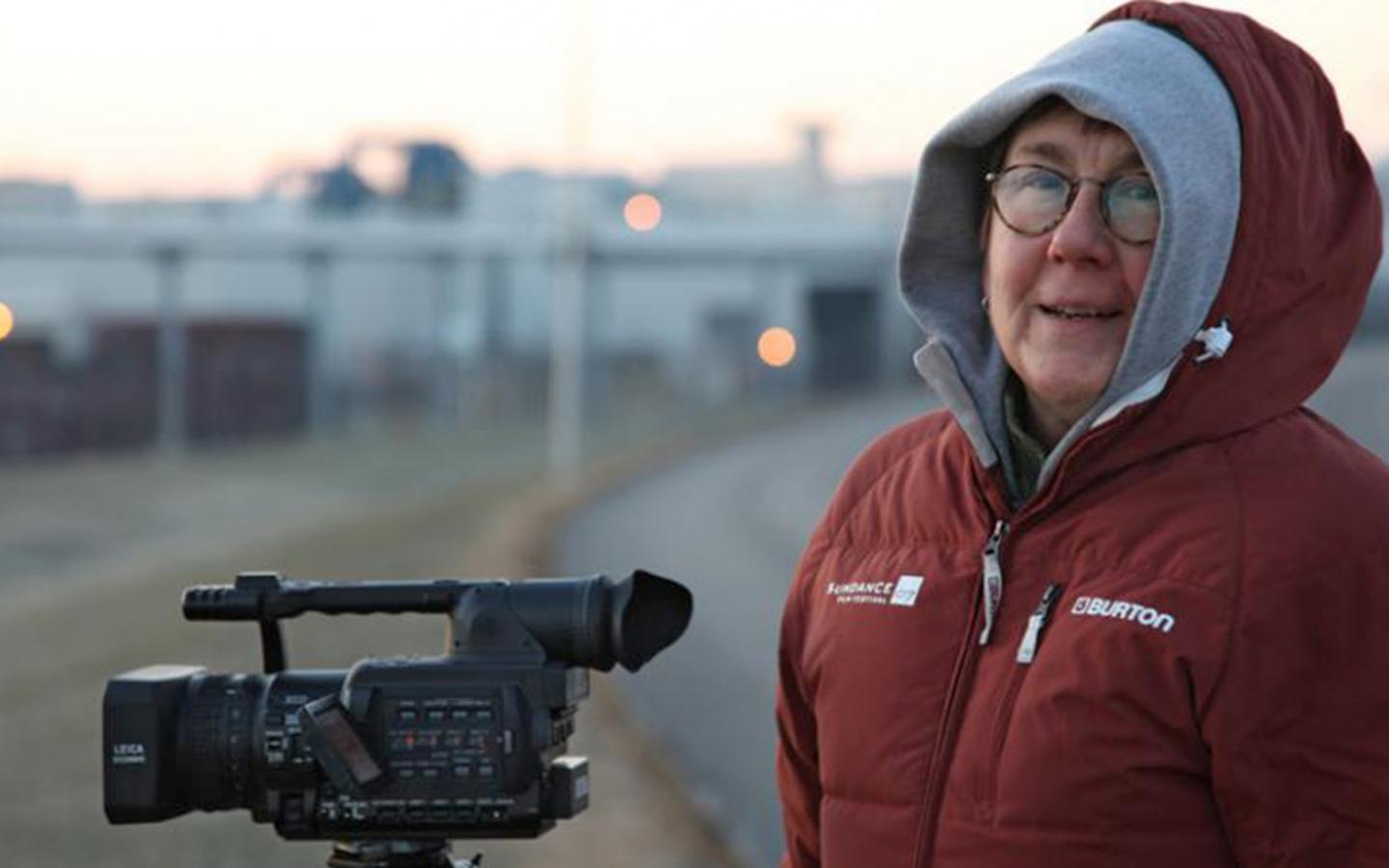 Filmmaker Julia Reichert outside on a cold morning with a video camera.