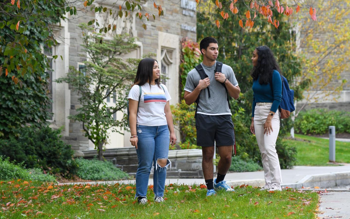 Three students standing and chatting outside with the ILR School in the background..