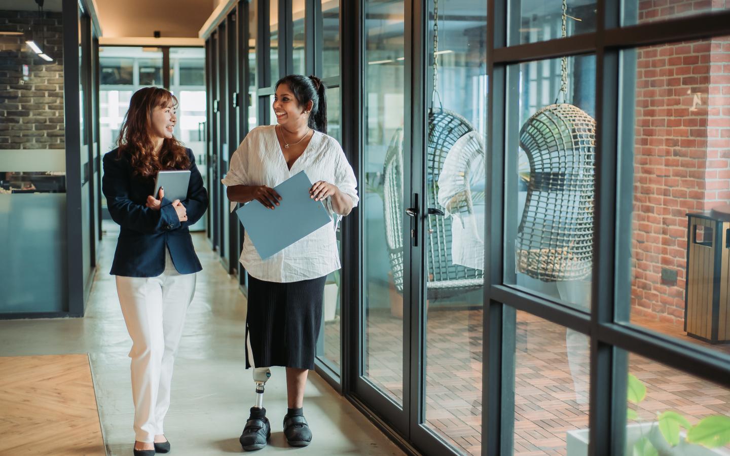 Two women at work walking and talking. One woman has a prosthetic leg.