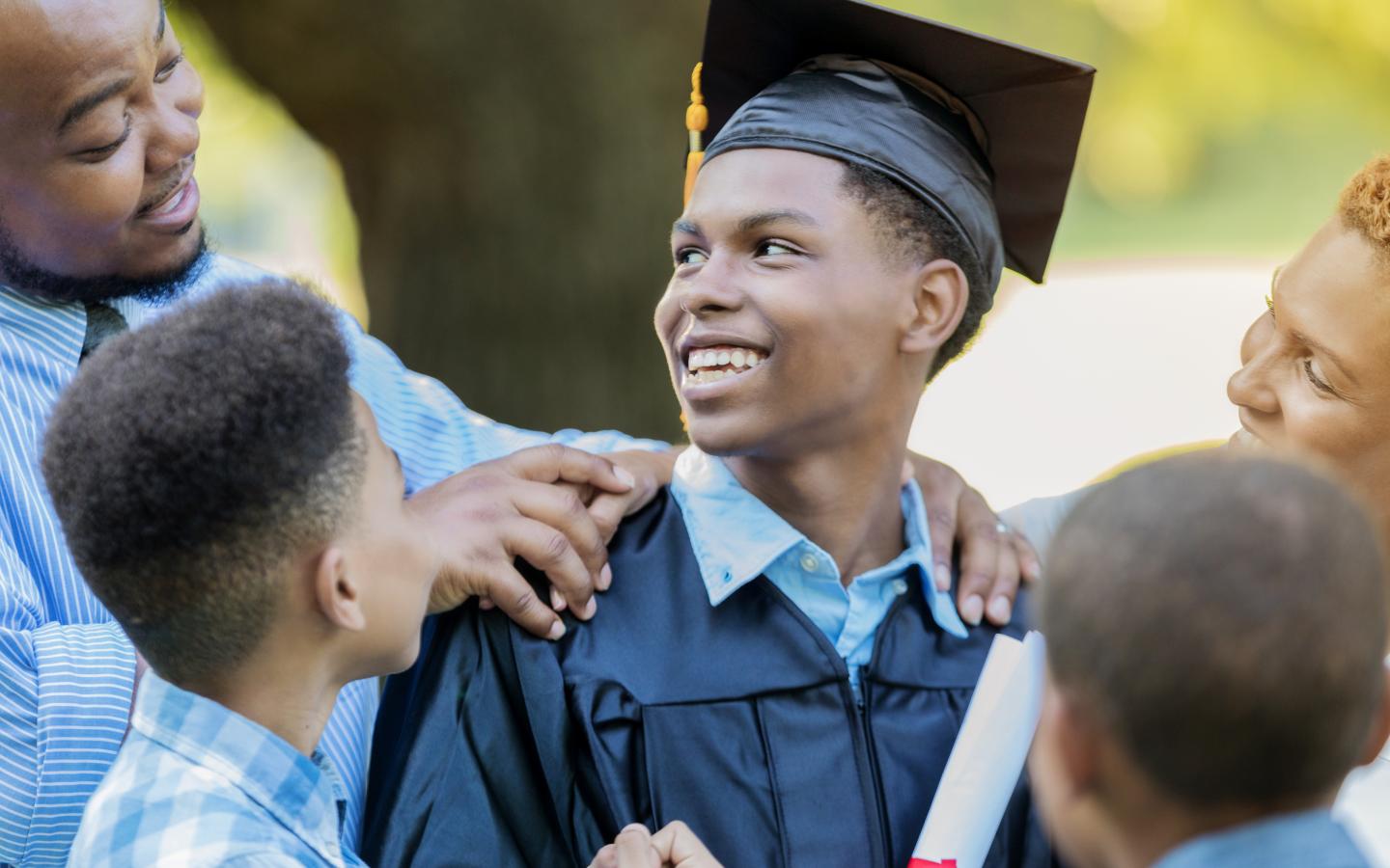 Student in graduation cap and gown smiling at family members surrounding him