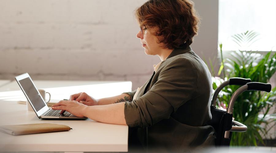 woman in a wheelchair working at a desk on a laptop computer