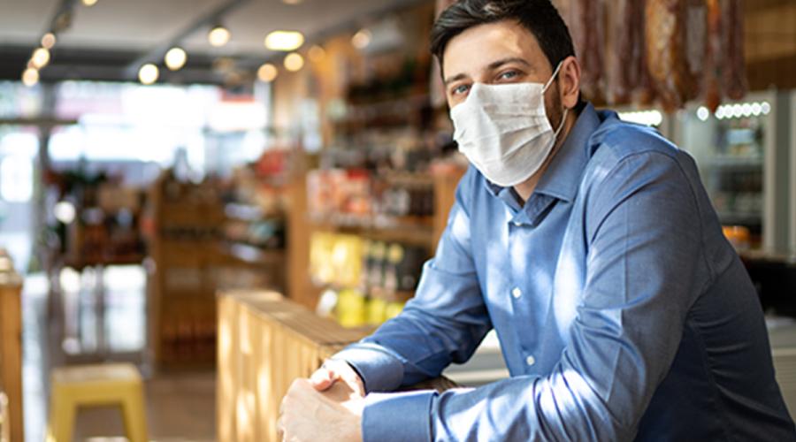 Man wearing a mask looking towards the camera with an empty restaurant in the background.