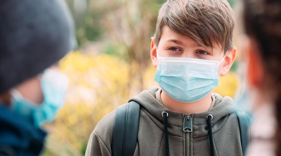 A young boy is wearing a medical mask talking with friends at school.