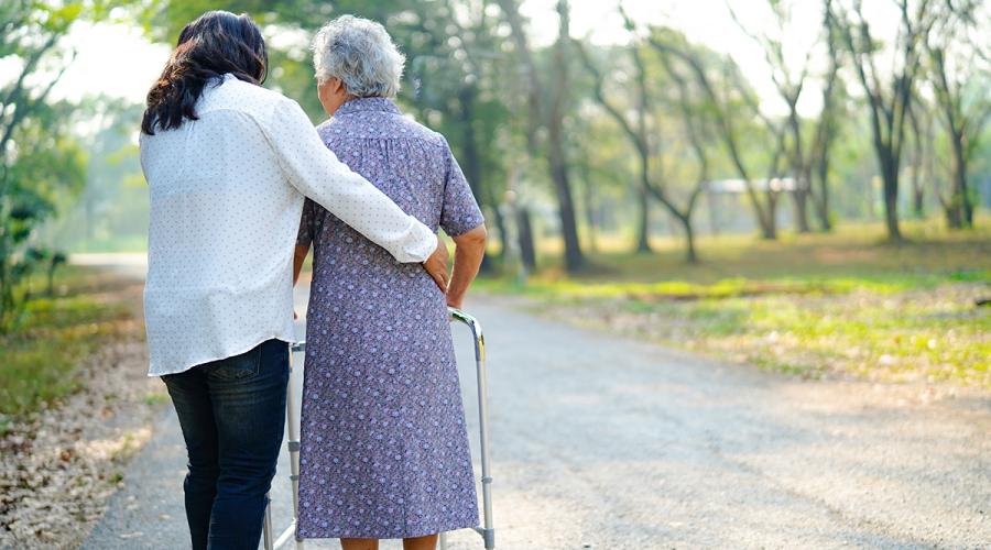 Older woman outside with a walker assisted by a home health aide