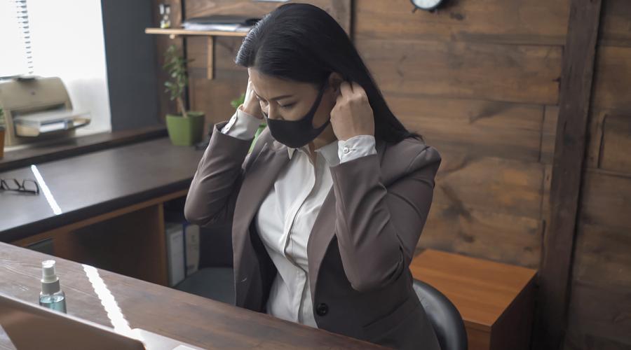 Woman sitting at a desk and adjusting her face mask.