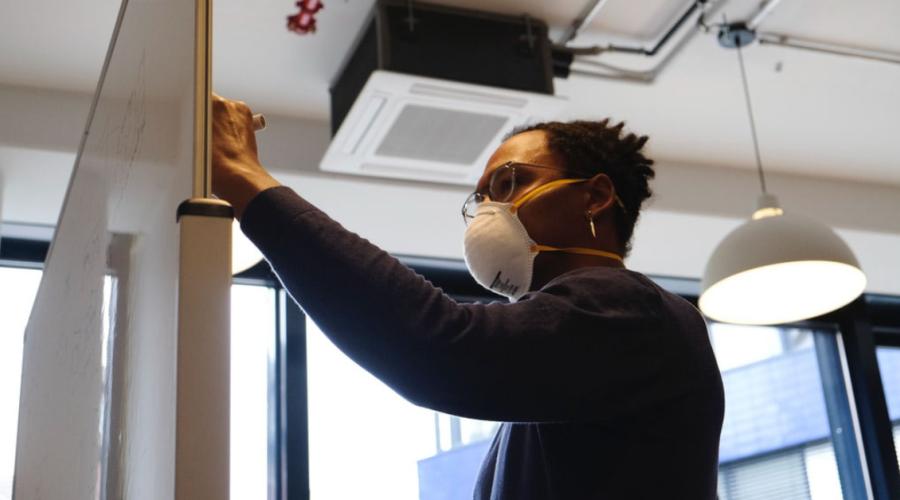 Worker writing on a whiteboard with a mask.