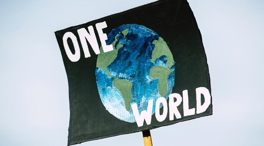 sign on a post saying: "one world" over a graphic of the globe to illustrate unity and the planet