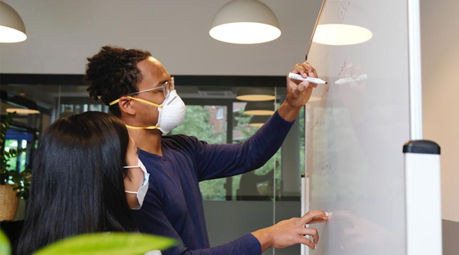 A young man and young woman working together at a whiteboard.