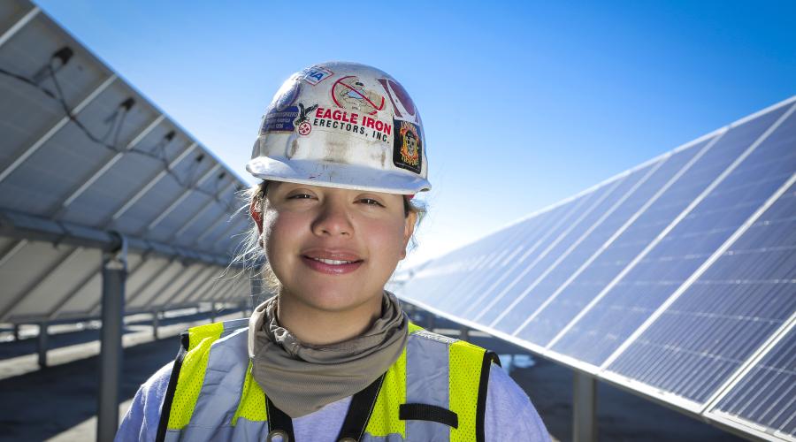 Union woman worker wearing a hard hat and standing in front of solar panels