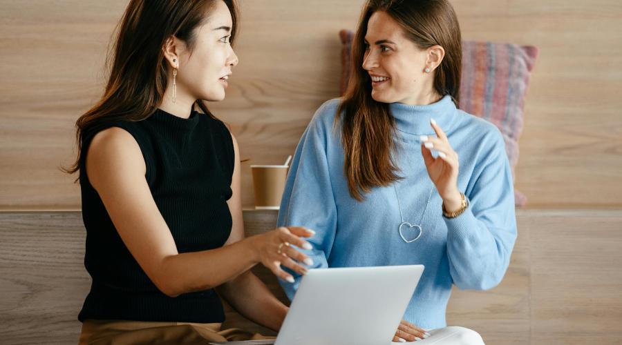 two women talking while sitting with a laptop in front of them