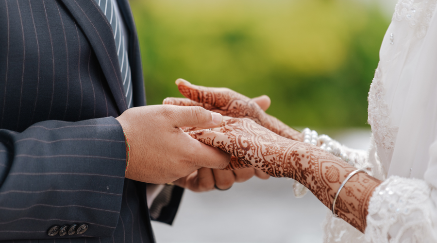 An image of a man and woman's hands at a wedding ceremony. The woman's hands are covered in henna tattoos.