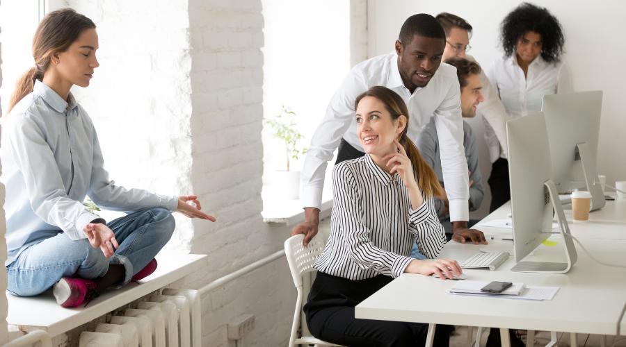 A young woman meditates while others participate in a meeting.