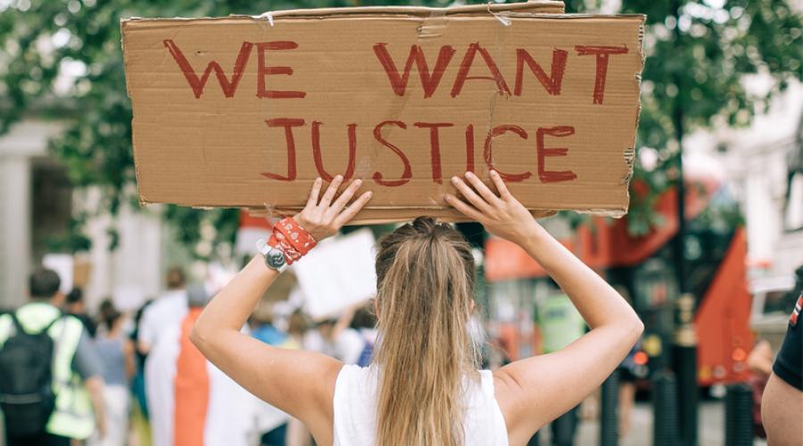 A young woman at a protest holds a sign that reads "We Want Justice"