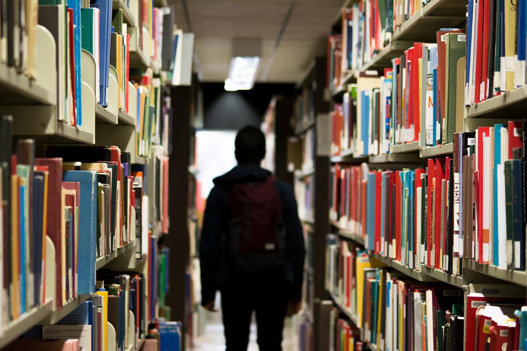 person walking through hallway lined with books