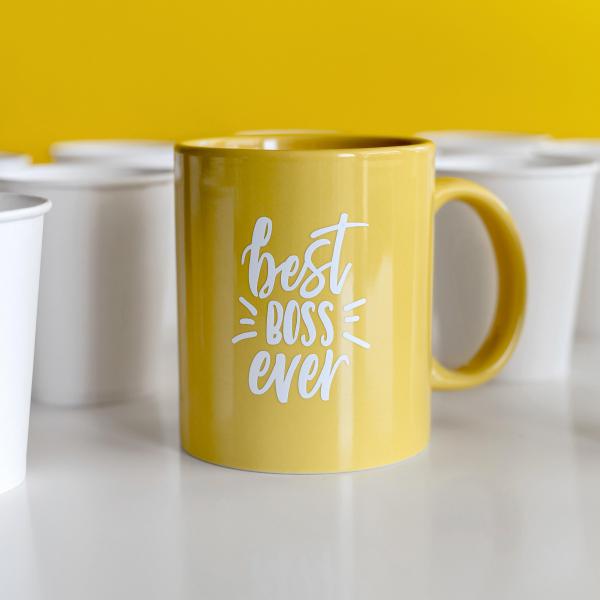 A yellow mug that says "Best Boss" sits among white paper coffee cups.