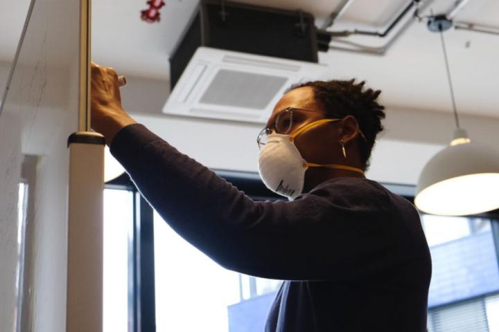 Worker writing on a whiteboard with a mask.