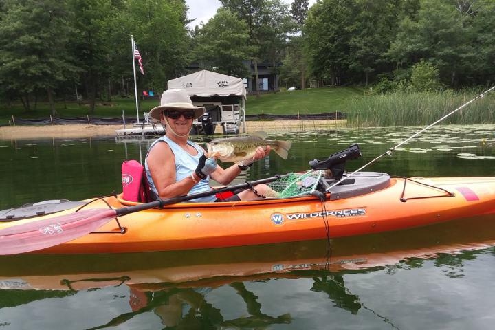 Andrea Dutcher sitting in a kayak on a lake holding a fish she caught.