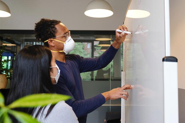 A young man and young woman working together at a whiteboard.