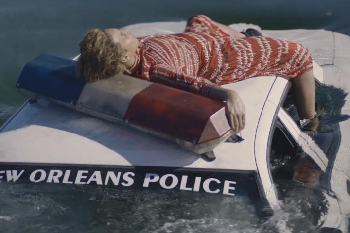 Person laying on a police car that says New Orleans Police which is sinking 