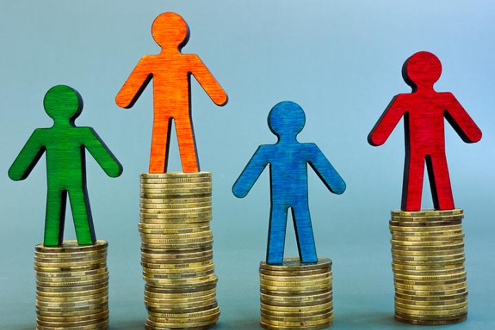 Pay inequality image of wooden figures standing on different size piles of money