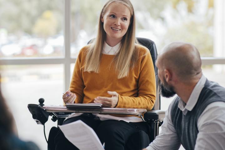 Young woman in a wheelchair talks with a co-worker