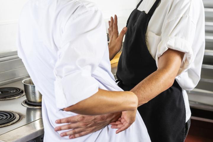 A male food service worker improperly touching a female colleague in a commercial kitchen. 