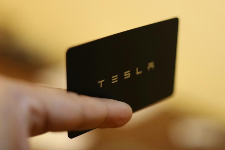 Hand reaching into frame extending a Tesla card 