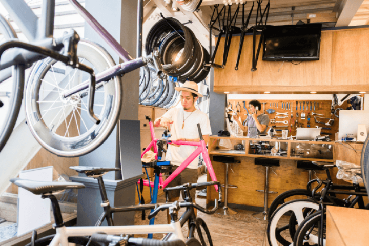 Two workers in a shop, surrounded by bicycle tires, tools, and equipment