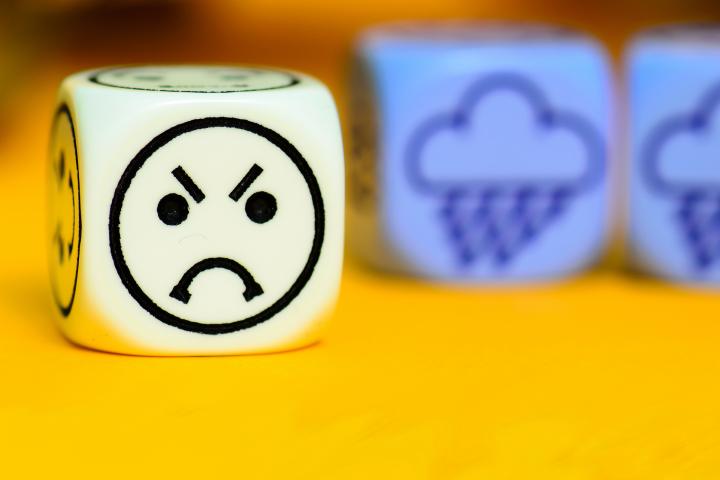 A six-sided die shows an angry emoji with two dice in the background showing rain clouds