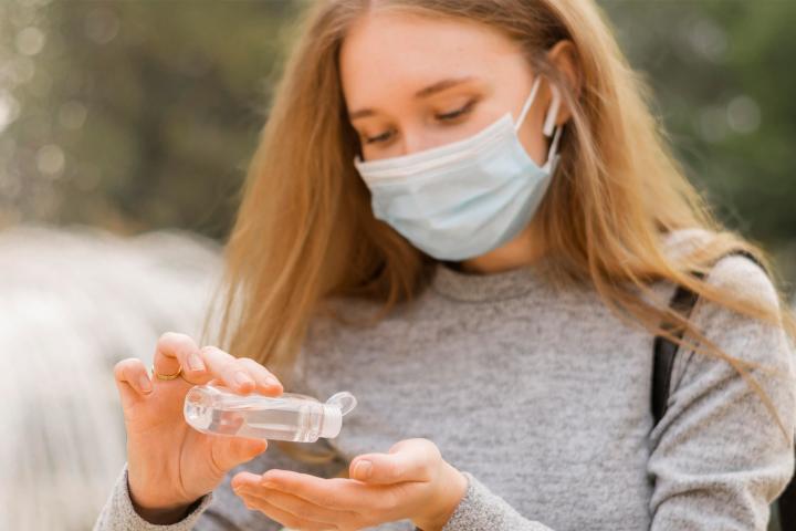 A woman wearing a mask applies sanitizer to her hands