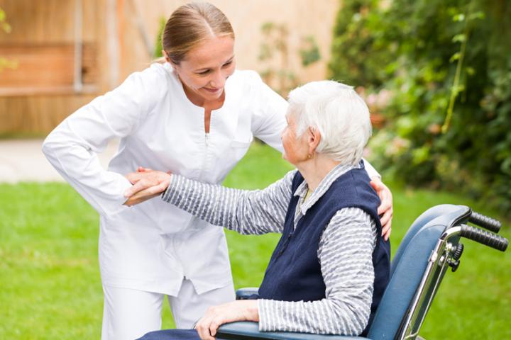 A home health care workers helps a patient out of her wheel chair.