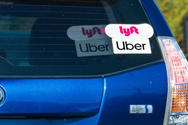 Uber and Lyft stickers on the back of a blue car.