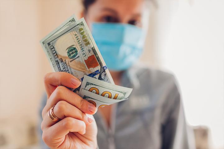 A woman in a medical mask holds cash towards the camera
