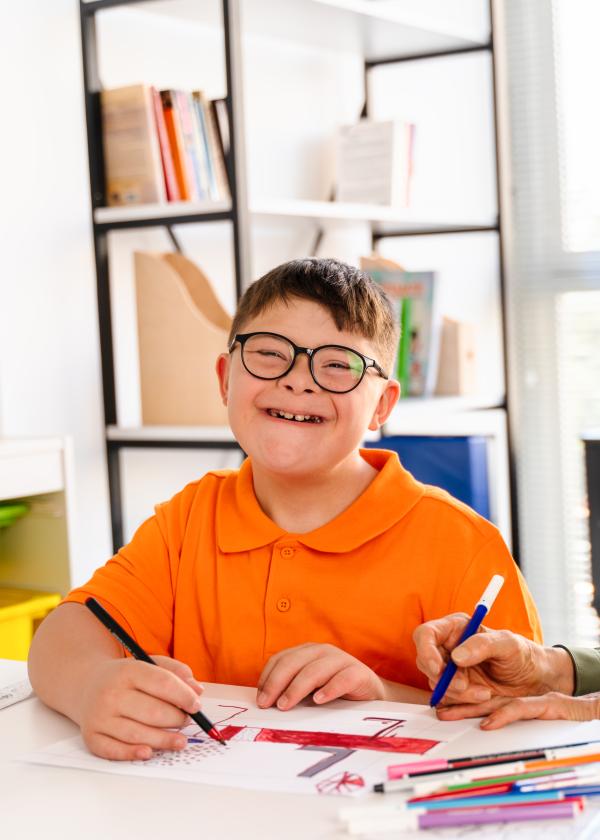 child with a disability smiling at a desk at school