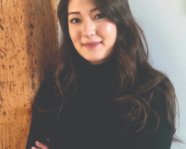 friendly and professional woman leans against wall with arms crossed looking at camera