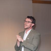 A man stands talking with his hands clasped